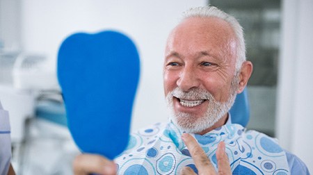 Man smiling while looking at reflection in handheld mirror