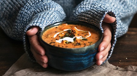 A closeup of hands holding a bowl of pumpkin soup