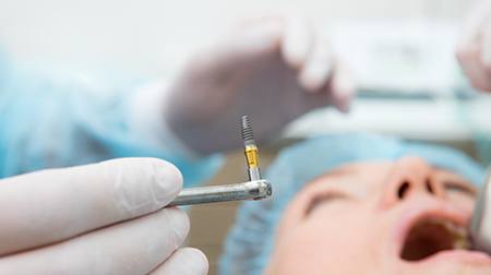 Oral surgeon about to place implant in patient’s mouth