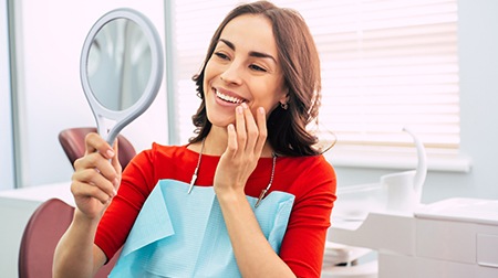 Woman in red-orange shirt smiling at reflection in dental chair