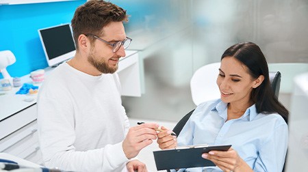 Man in white handing pen to patient in dental chair to fill out forms