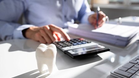Someone working at desk with invoices, calculator, and large model tooth