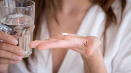 Woman holding glass of water and a pill