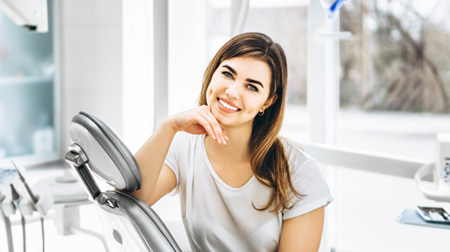 Female patient in treatment chair smiling and resting chin on hand